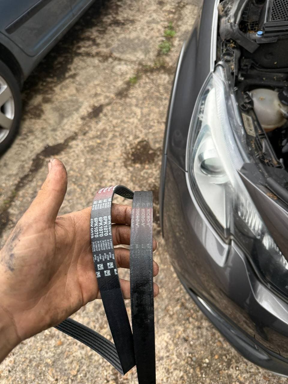 A new auxiliary belt held beside the old one in front of the car