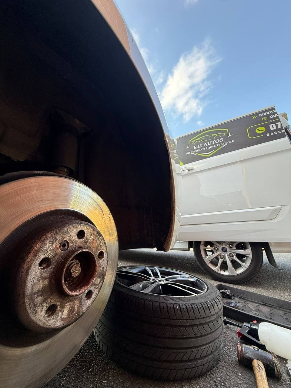 A bare brake disc with the wheel off and alloy wheels stacked alongside