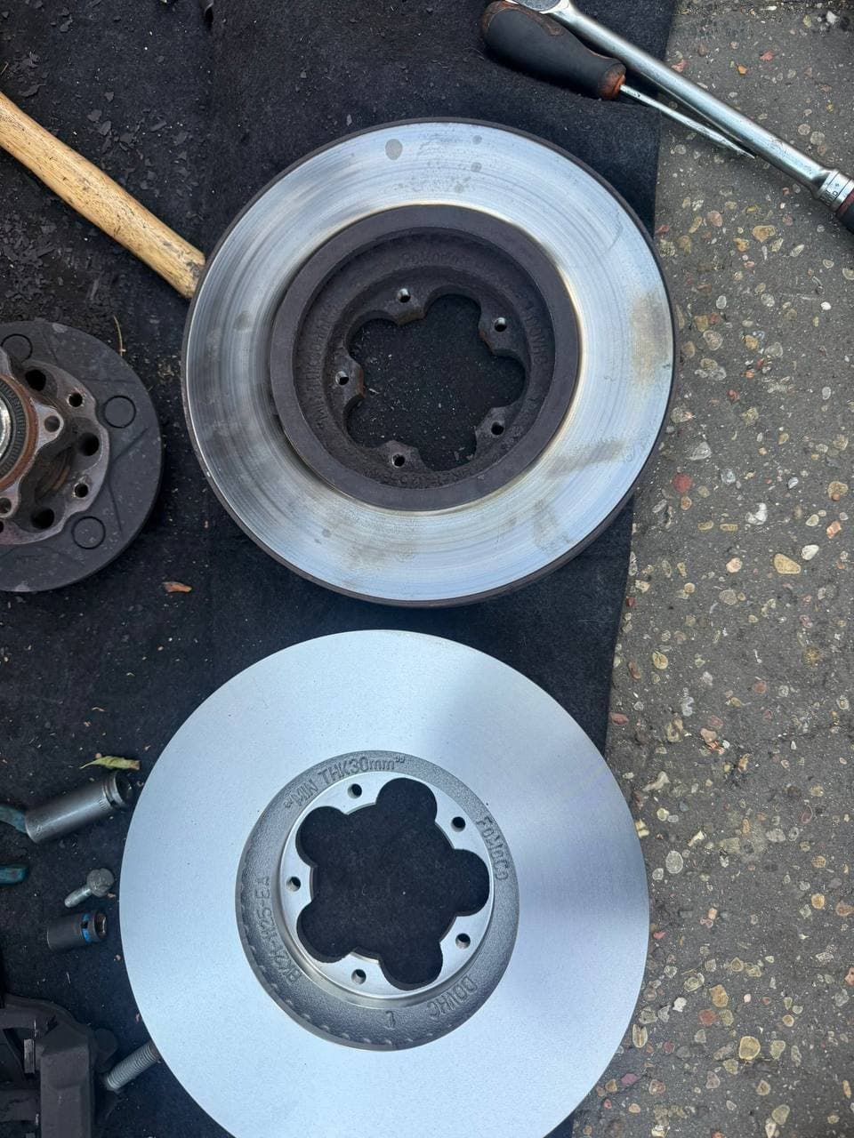 A worn brake disc beside the new one replacing it, with the tools for the job