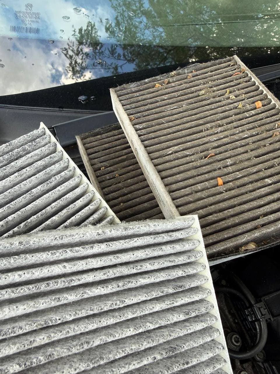 Clogged cabin filters resting on a windscreen beside a clean replacement