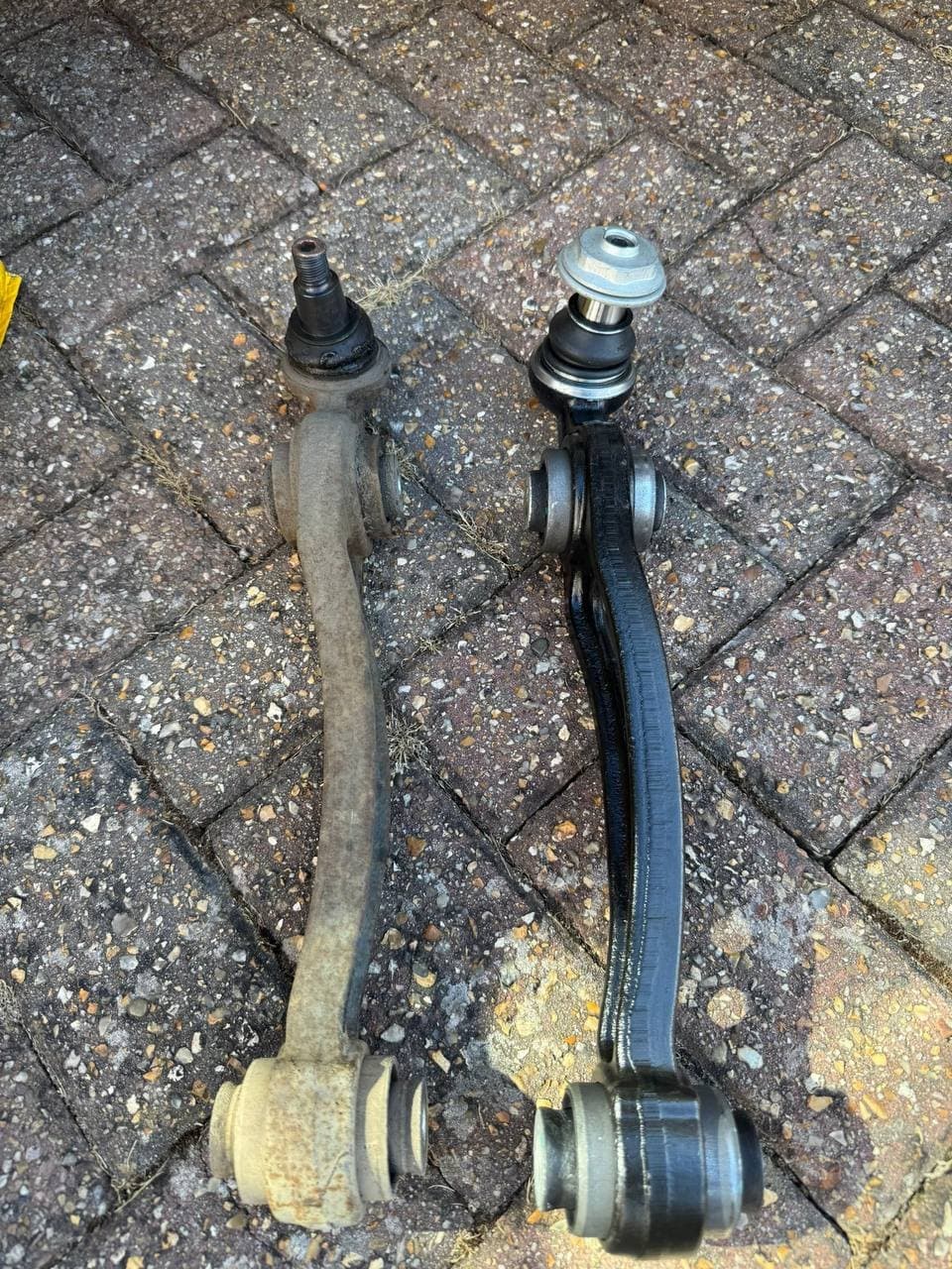 A new front control arm beside the corroded one it replaced