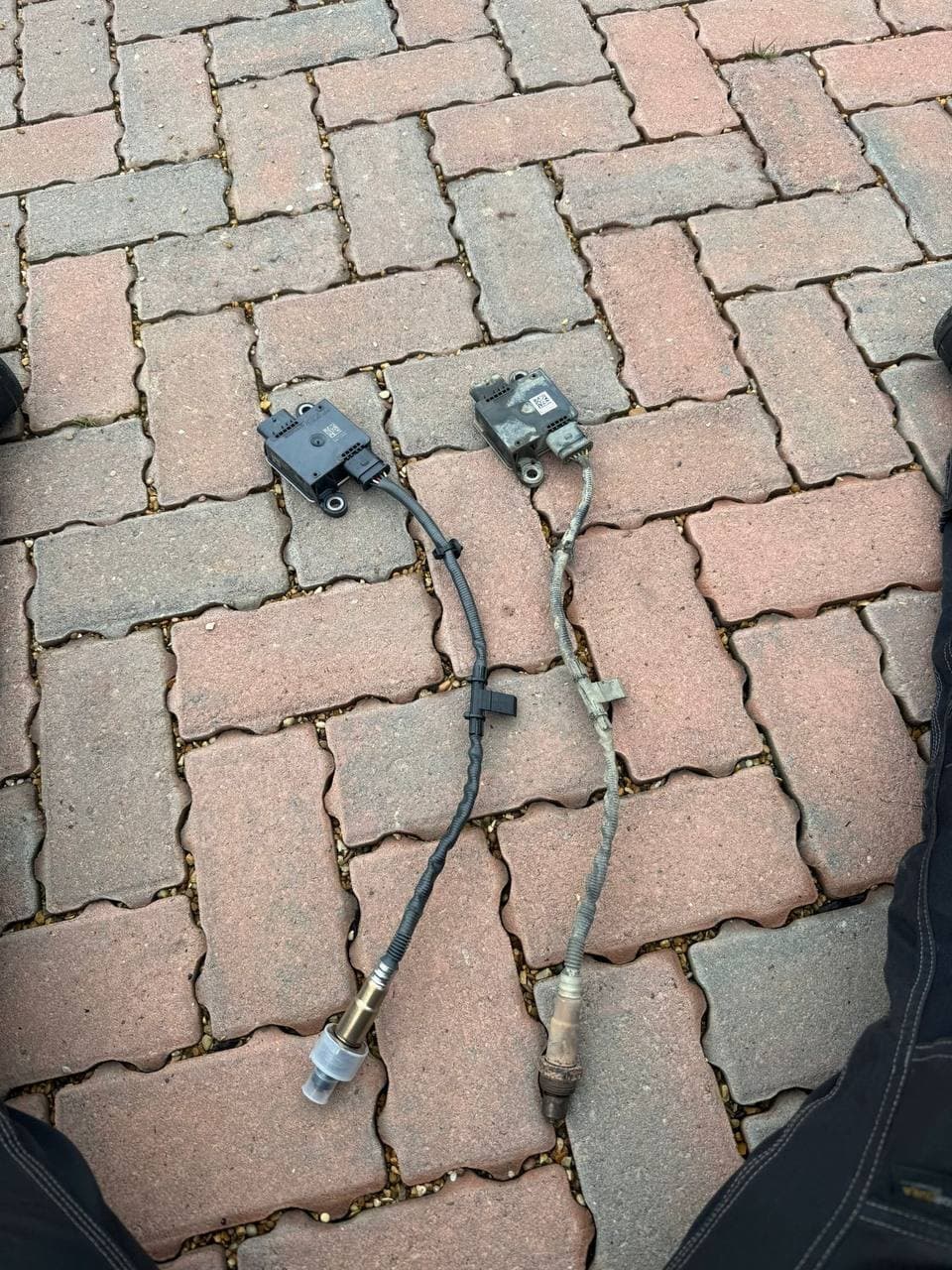 Two exhaust gas sensors laid out on a driveway, the old one and its replacement