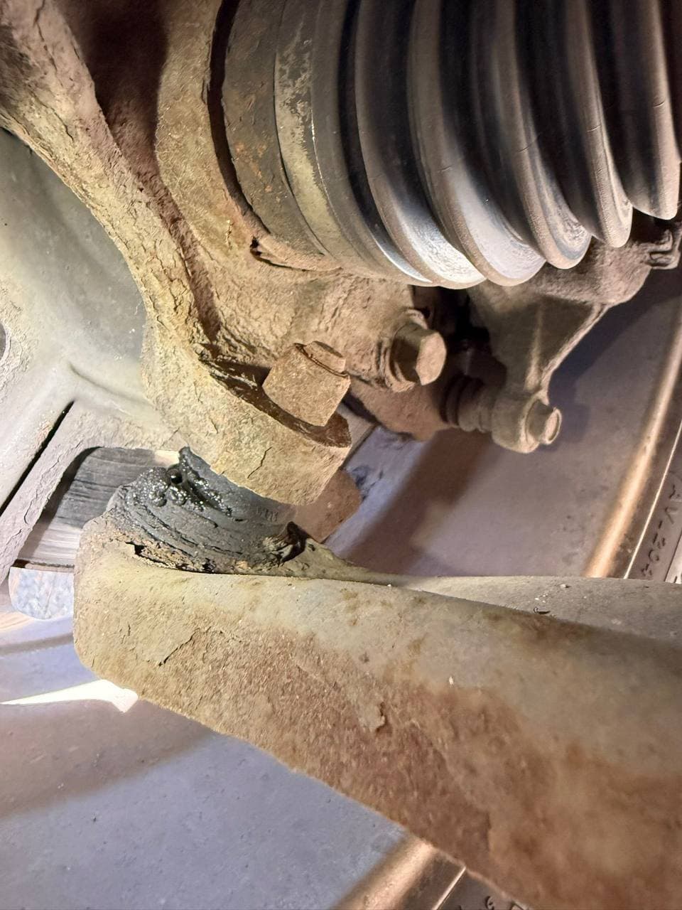 A perished suspension bush on a corroded lower arm, seen from underneath