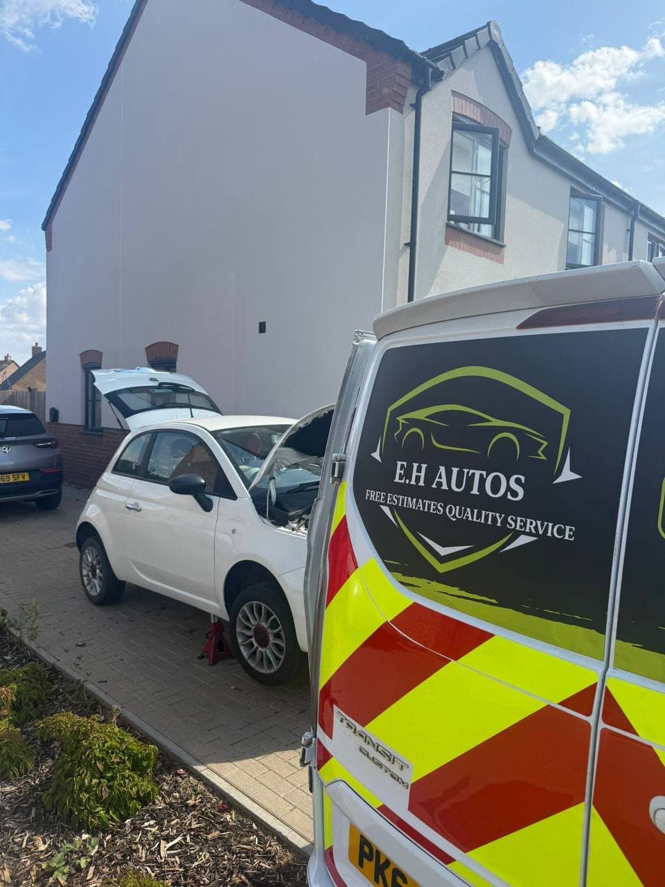 The EH Autos van beside a car raised on a jack on a driveway