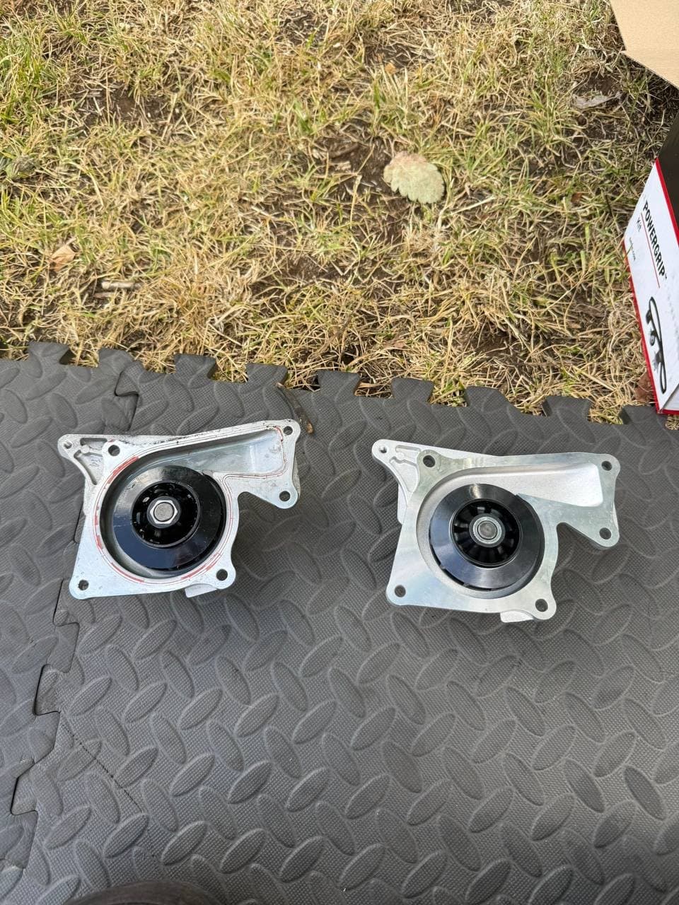 A new water pump beside the old one, with the belt kit box alongside