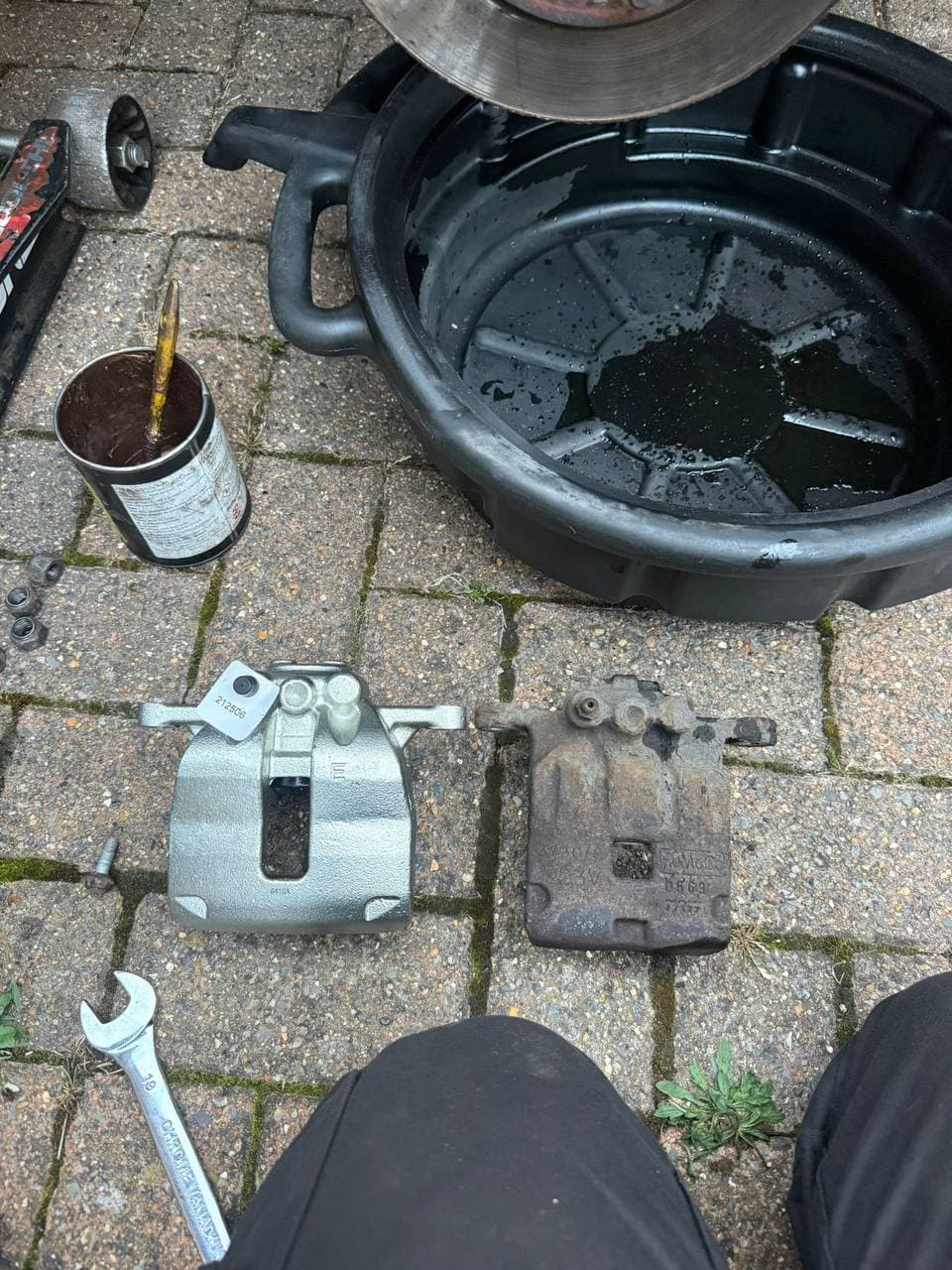 A new brake caliper on the ground beside the corroded one it replaced
