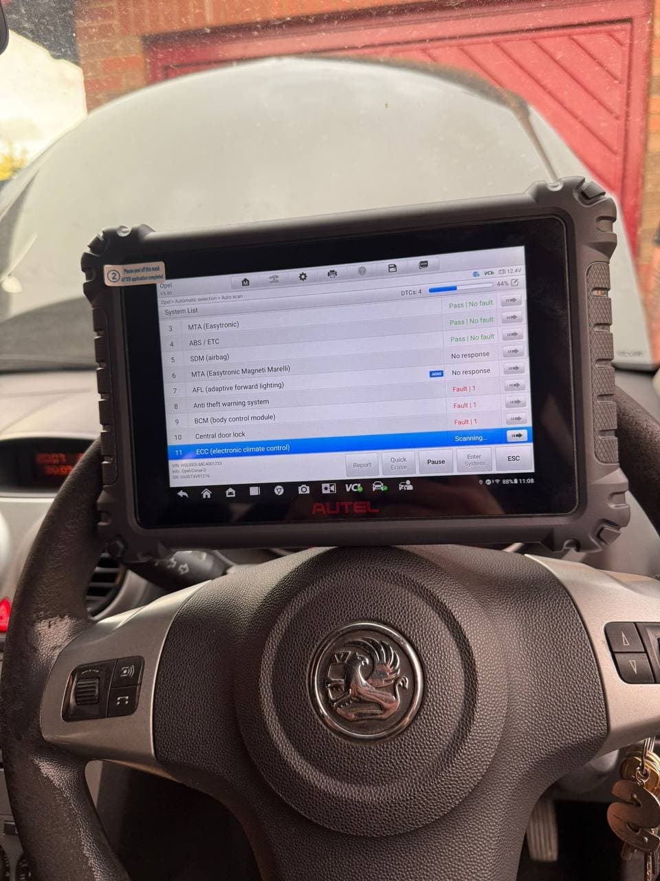 A diagnostic tablet running a full system scan, propped on a car's steering wheel