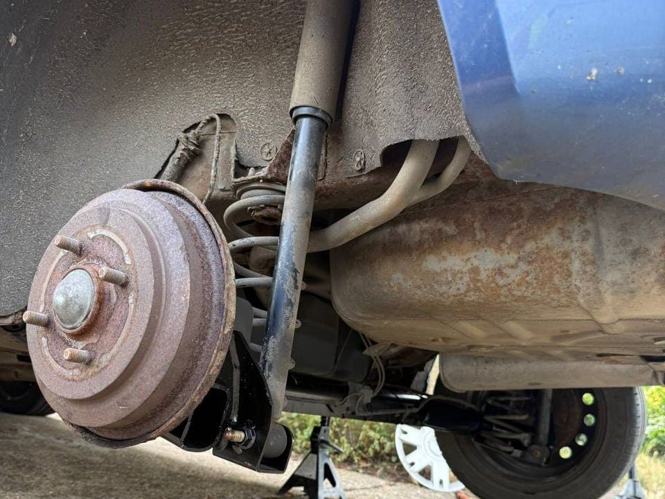 The underside of a car on an axle stand, showing the rear brake, shock absorber and exhaust